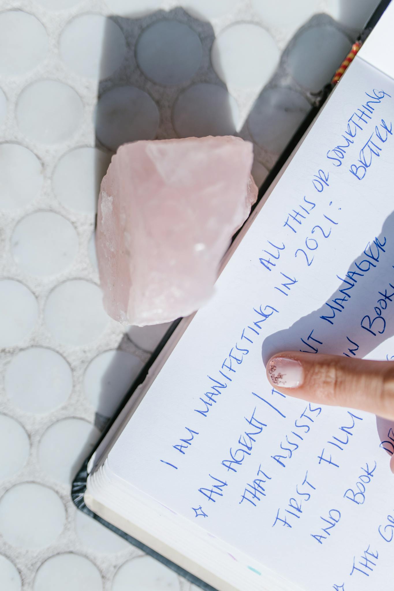 Close-up of a manifestation journal page with a rose quartz crystal and finger pointing.