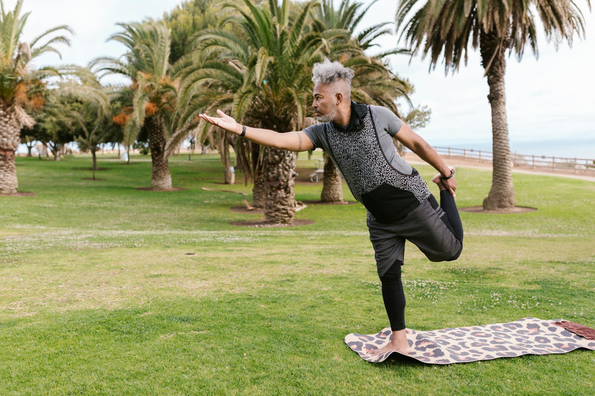 Elderly man performing yoga on a mat in a green park, promoting wellness and balance.