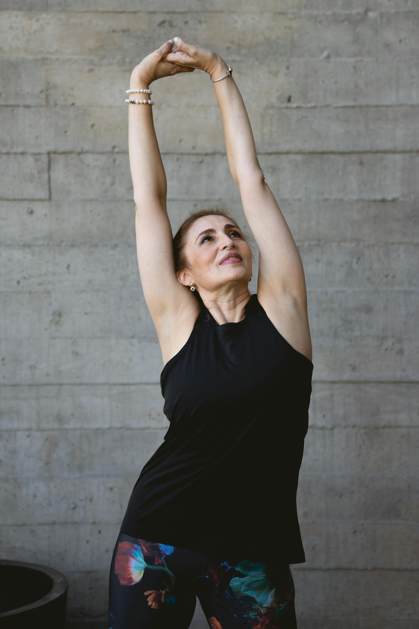 Elderly woman in black tank top stretching indoors for fitness and positive aging.
