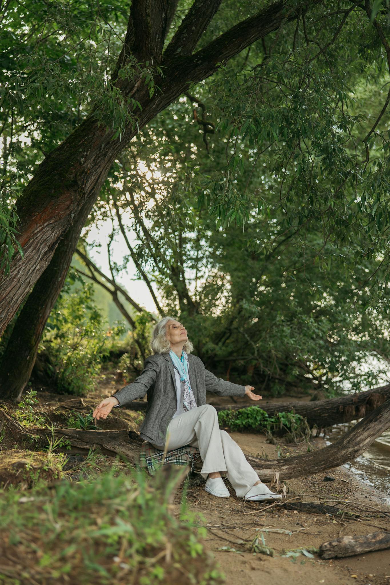 Elderly woman seated under a tree, embracing nature, showcasing freedom and serenity.